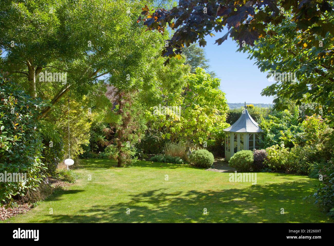 Gazebo ottagonale circondato da alberi in giardino maturo con prato e swing in estate Foto Stock