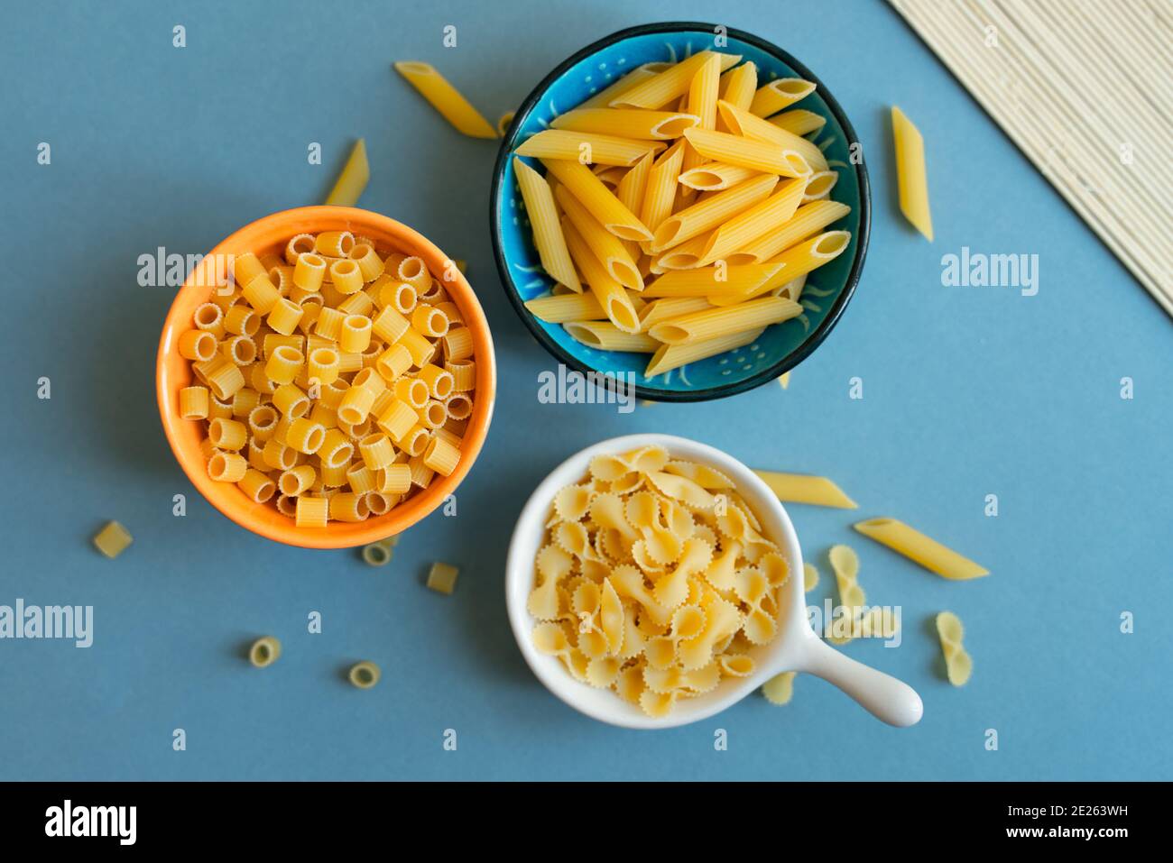 penne, farfalle tonde butterfly e ditalini tipo di pasta su fondo azzurro. pasta in ceramica. ciotola blu arancio bianco. astratto, pasta. t Foto Stock