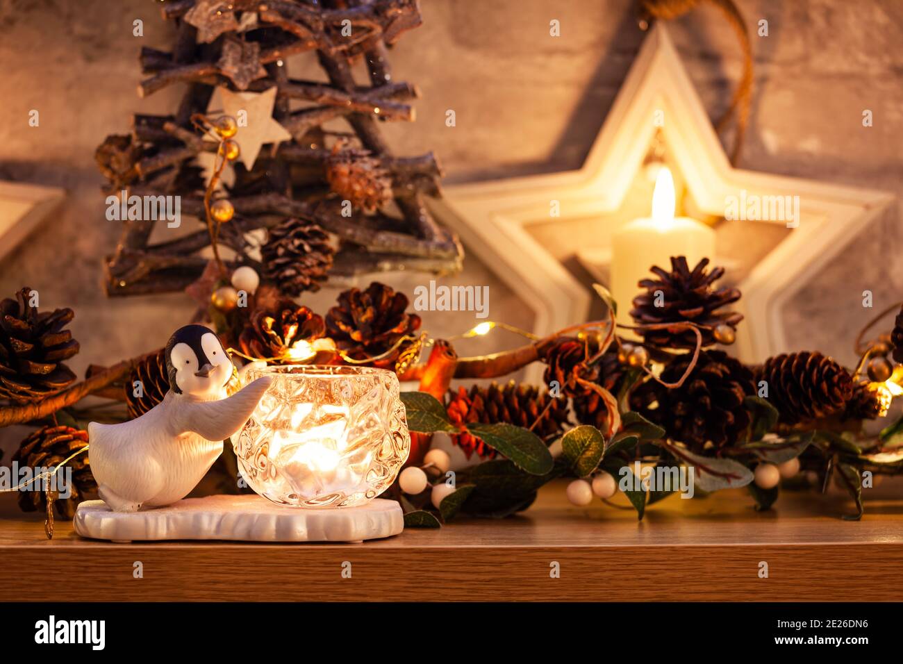 Penguin accanto a una candela su un pezzo di mannola con Natale pinecone ghirlanda e foglia d'oro fata luci Foto Stock