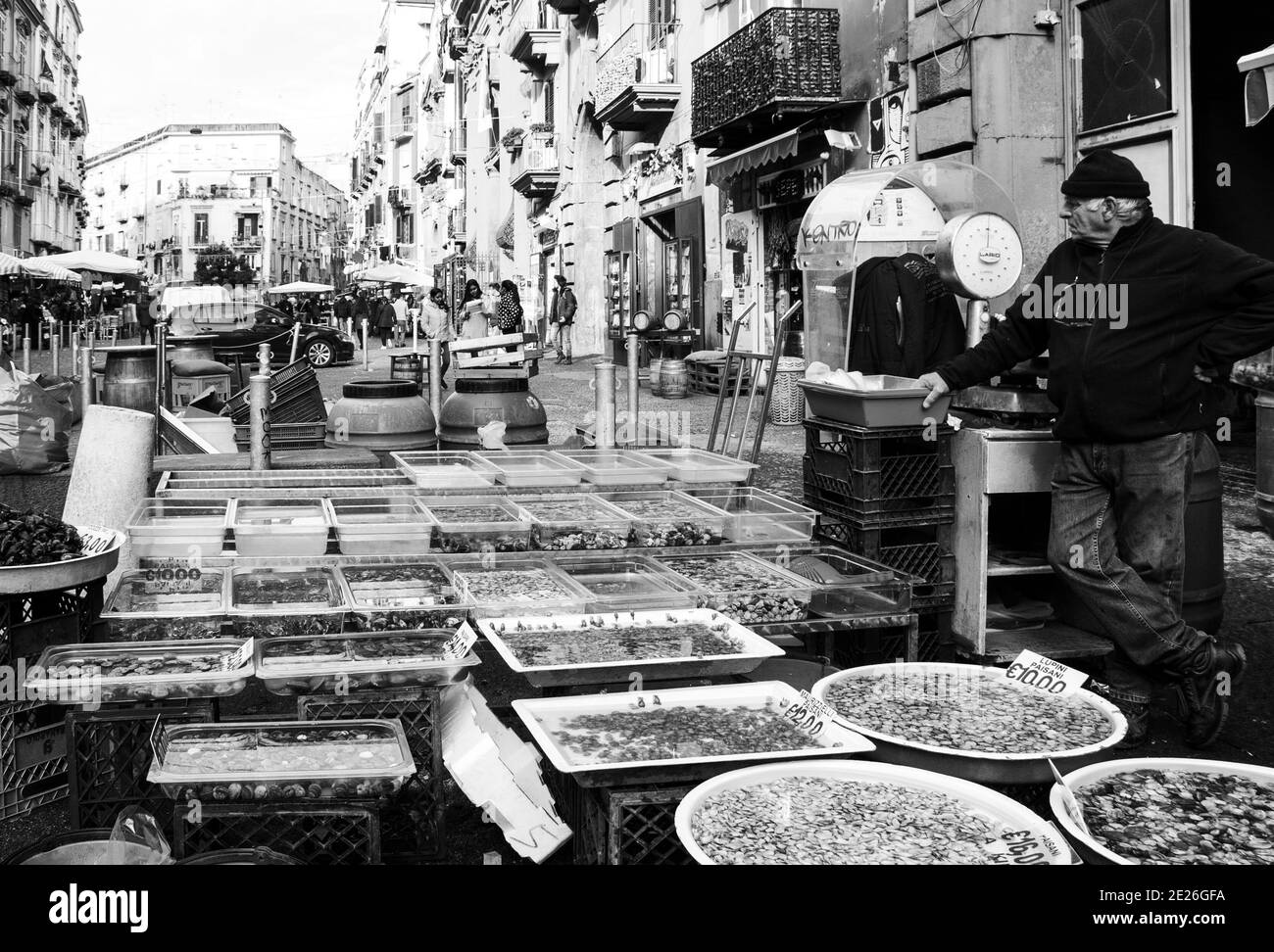 NAPOLI - 15 DICEMBRE 2019: Mercato di strada. Uomo anziano che vende frutti di mare - varietà di vongole fresche, crostacei, ecc Black bianco foto. Foto Stock
