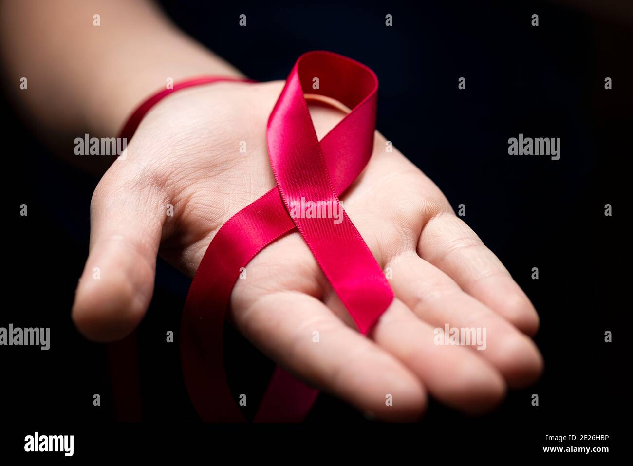 Nastro rosso nelle mani della donna su sfondo scuro per il concetto della Giornata Mondiale dell'AIDS. Foto Stock