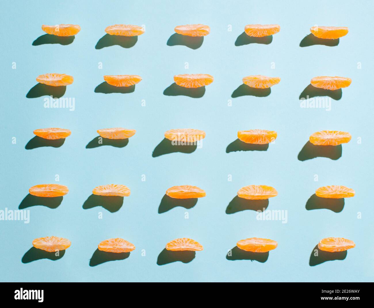 Motivo creativo con fette arancioni di mandarino su sfondo blu intenso. Posata piatta minima illuminata dal sole. Foto Stock