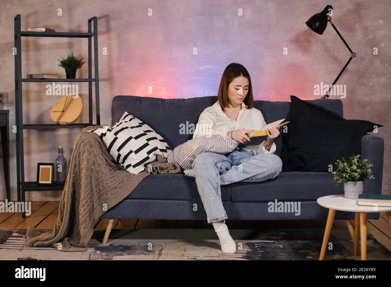 Giovane ragazza asiatica che legge un libro. La ragazza è seduta sul divano. Camera accogliente. Foto Stock