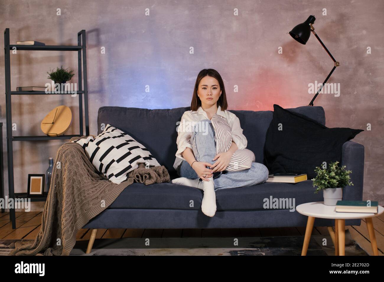 Una donna seduta su un divano in un accogliente camera a guardare la TV e sconvolto da ciò che vede sullo schermo Foto Stock
