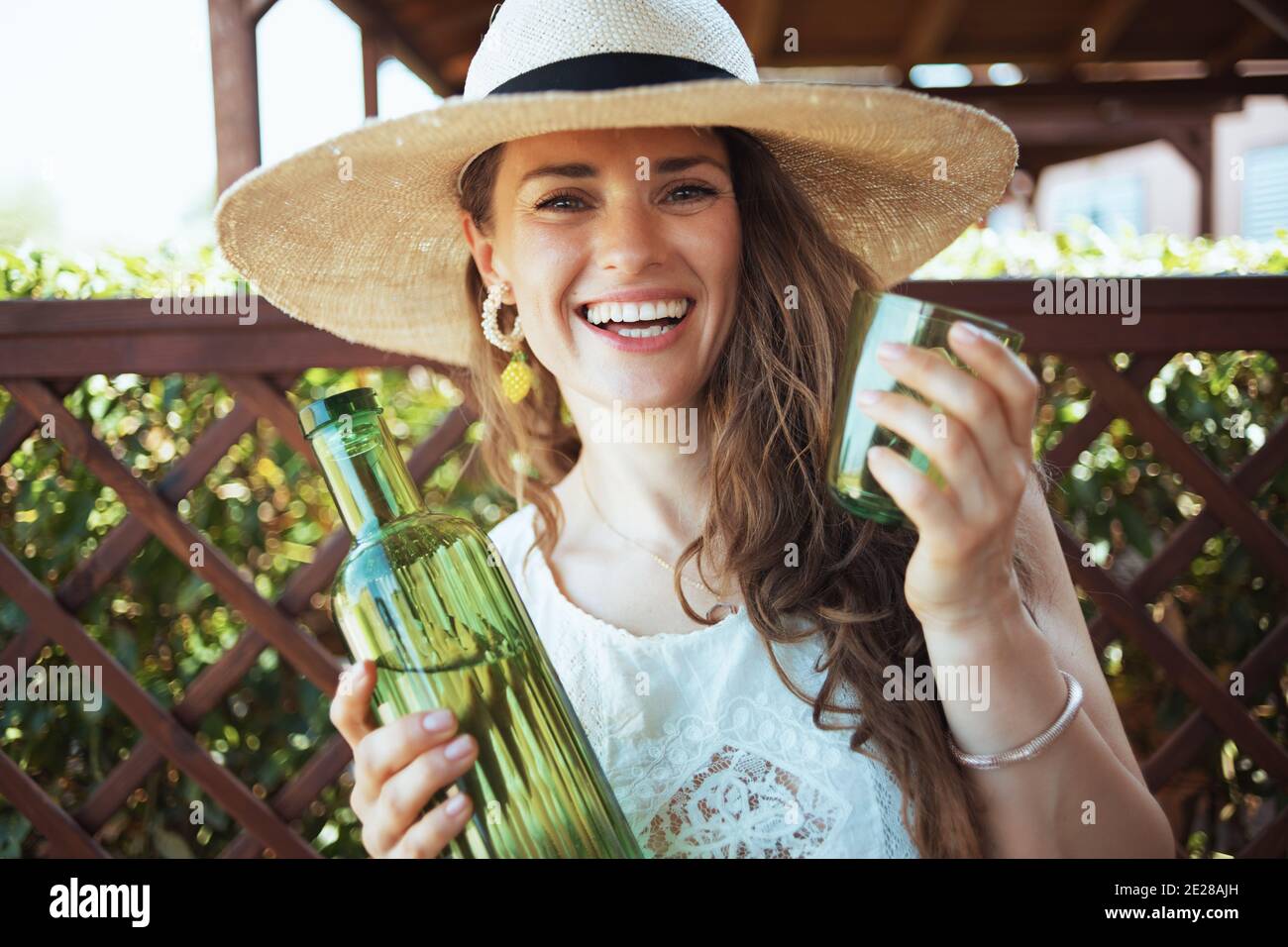 Ritratto di casalinga felice di mezza età in camicia bianca con bottiglia d' acqua, vetro e cappello nel patio Foto stock - Alamy