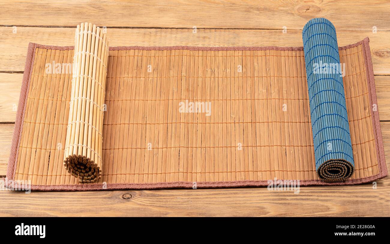 Tre stuoie da cibo su sfondo di legno. Due tappetini arrotolati. Utensili da cucina tradizionali. Foto Stock