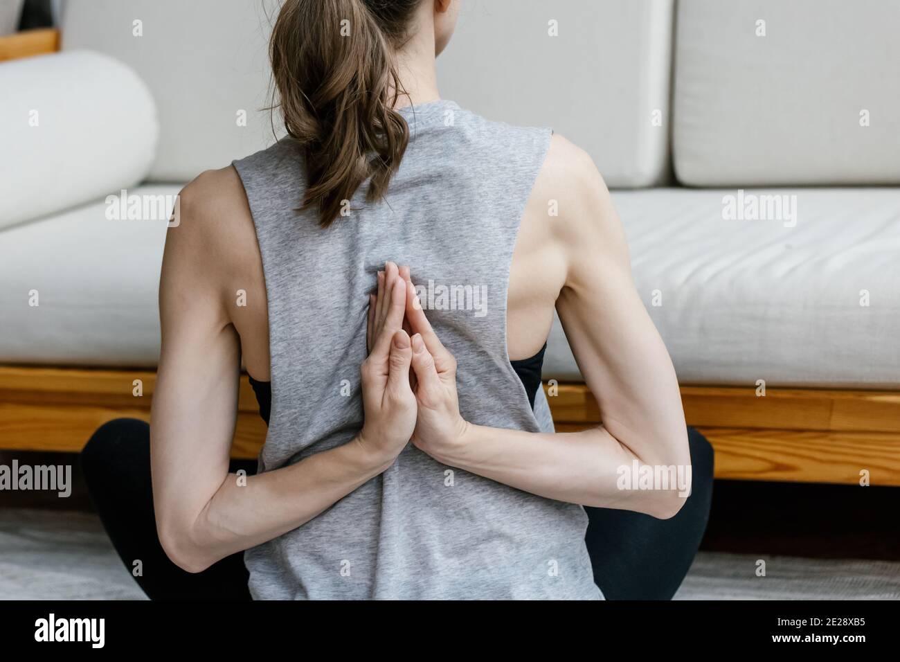 Giovane donna che fa yoga seduto in esercizio a casa sfondo interno. Vista posteriore immagine di una bella giovane donna che si prepara ad allenarsi a casa Foto Stock