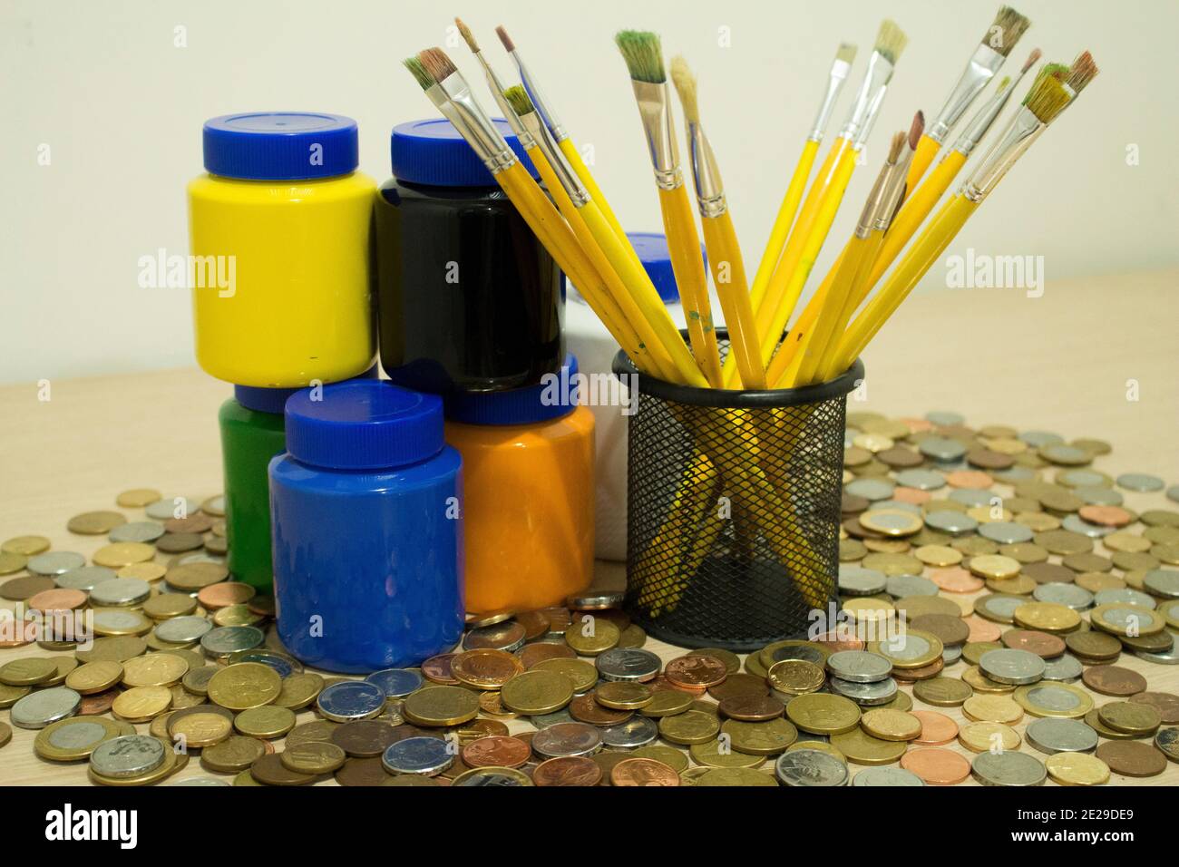 Dettagli di molti pennelli e diversi colori di vernice circondato da un sacco di monete su un tavolo Foto Stock