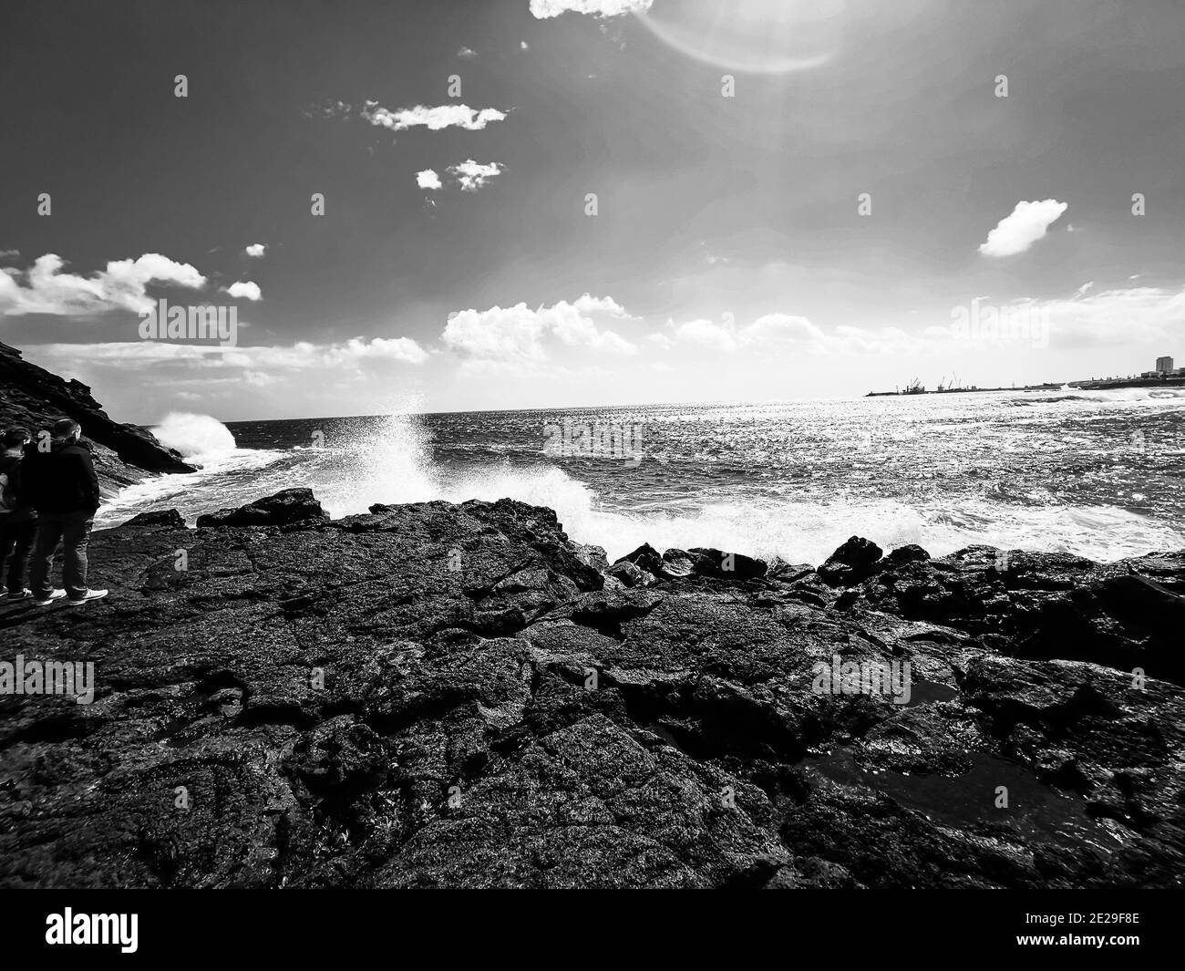 In scala di grigi di un mare dalla costa rocciosa in una giornata di sole, le onde si infrangono sulla riva Foto Stock