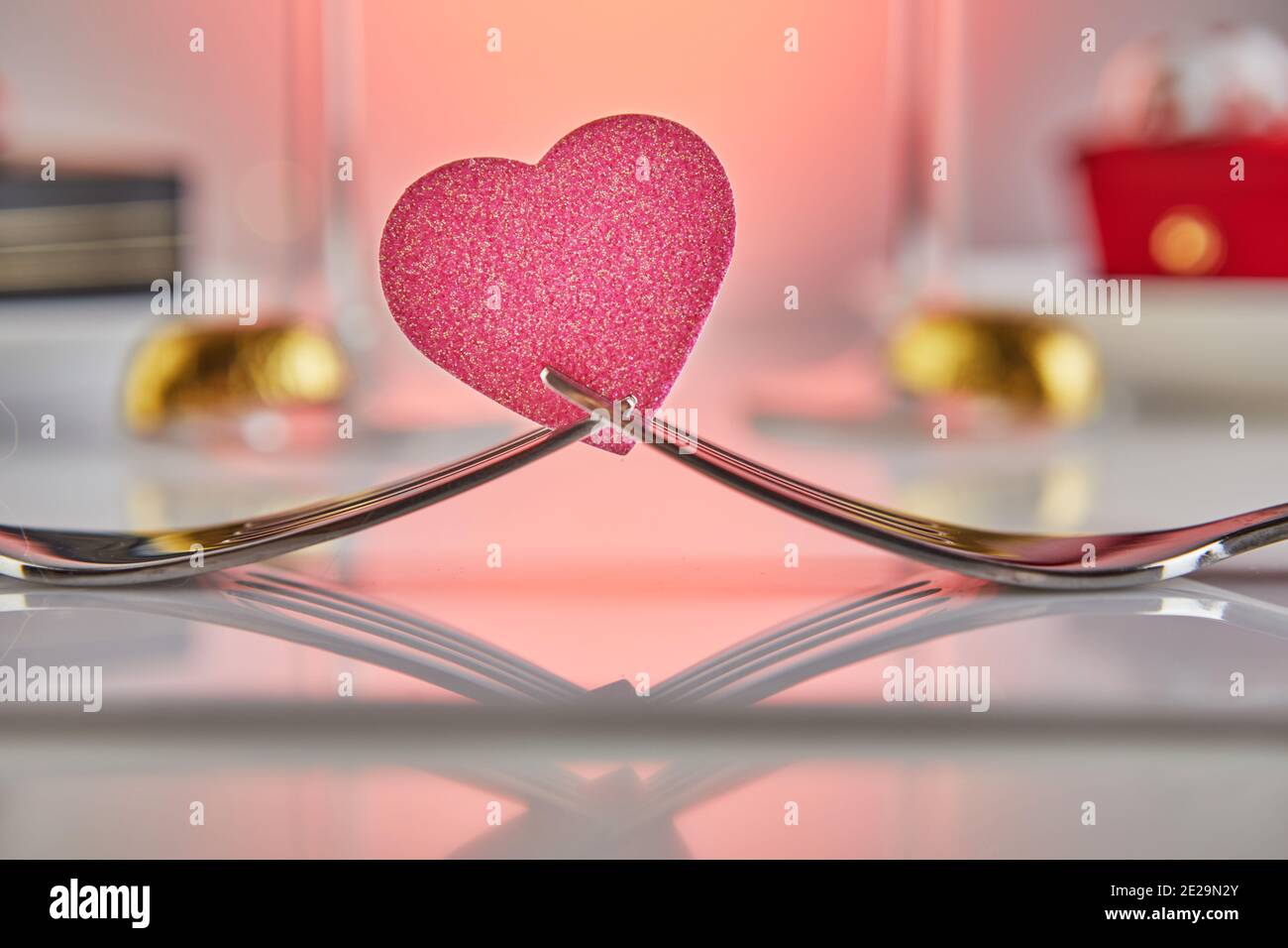 San Valentino o romantica cena di compleanno con cuori di caramelle, bicchieri di champagne e un elegante tavolo con riflessi Foto Stock