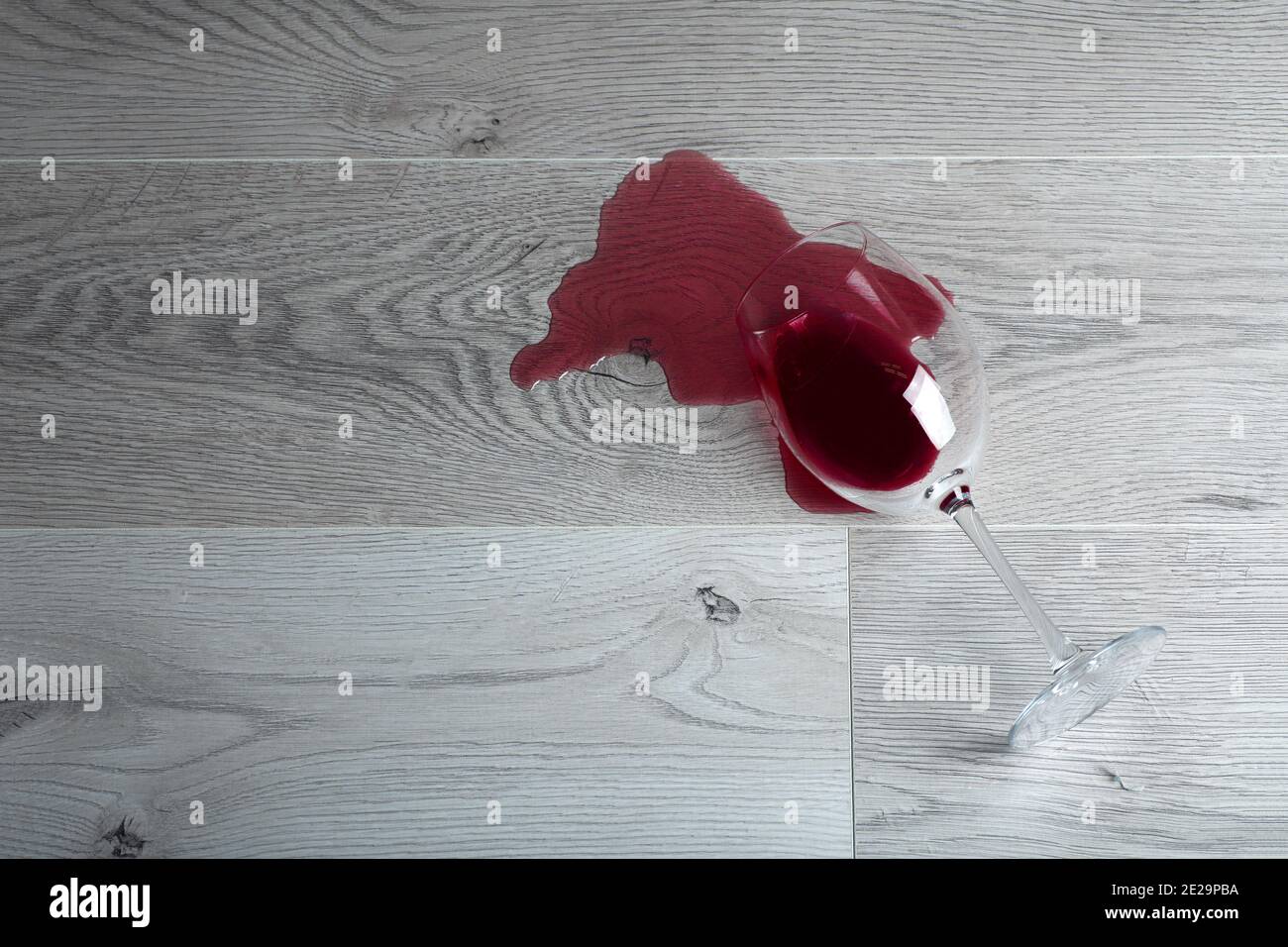 Pavimento in legno con bicchiere rovesciato di vino rosso. Vino versato su un pavimento in laminato di legno (parquet) con protezione dall'umidità. Foto Stock