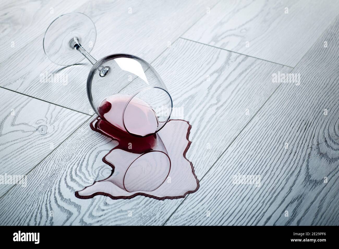 Pavimento in legno con bicchiere rovesciato di vino rosso. Vino versato su un pavimento in laminato di legno (parquet) con protezione dall'umidità. Foto Stock