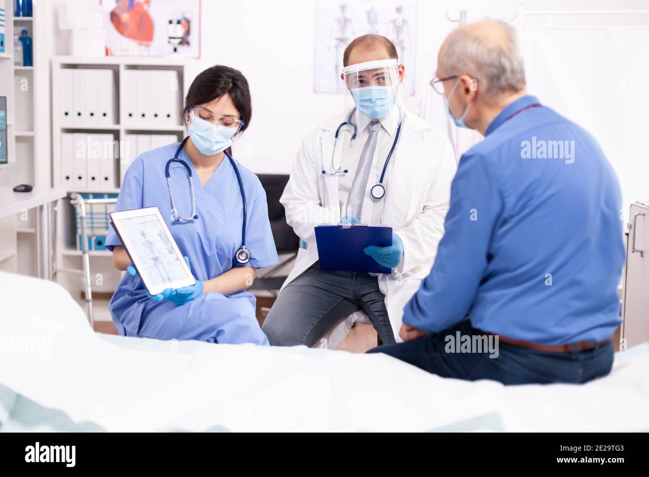 Medico sanitario che spiega l'anatomia umana all'uomo anziano mostrando PC tablet in tempo di pandemia di covidio. Personale medico in uniforme discutere di lesioni ossee con il paziente durante l'epidemia di coronavirus. Foto Stock