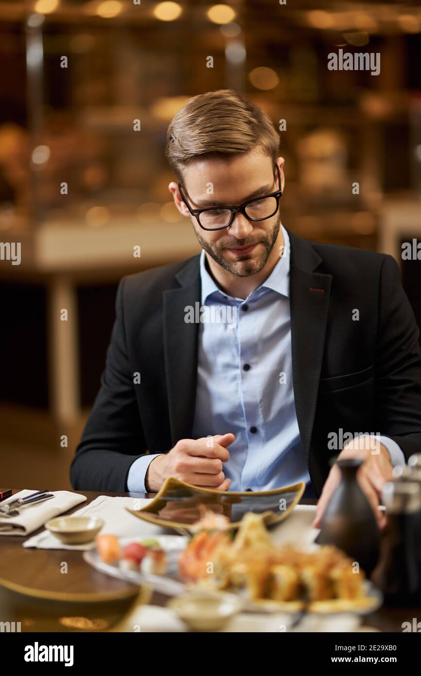 Uomo serio ed elegante in un bel vestito seduto al ristorante tavolo e controllare il suo argenteria Foto Stock