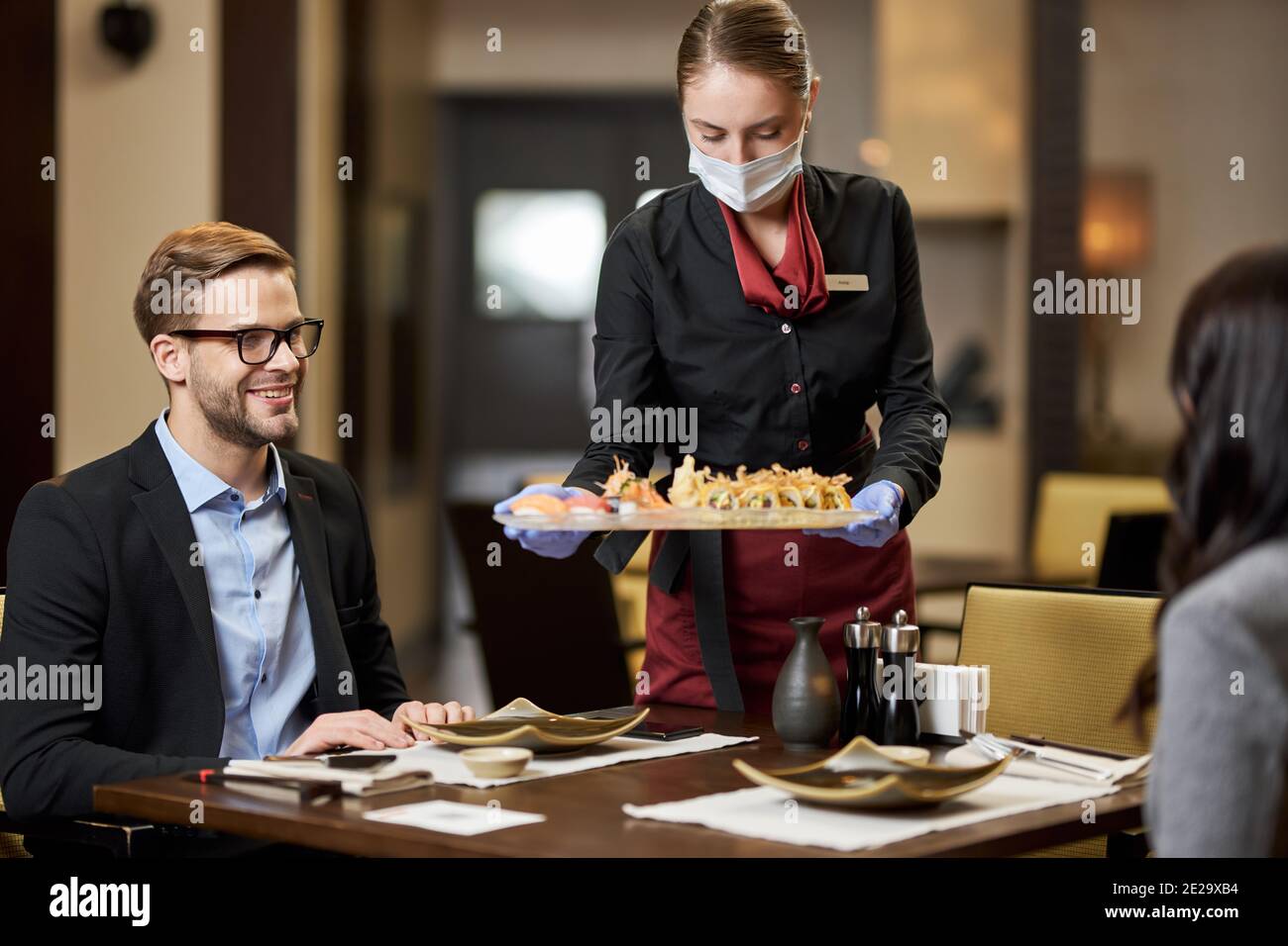 Il giovane si è accontentato di cenare con una signora mentre era professionale cameriera in maschera servendo loro sushi Foto Stock
