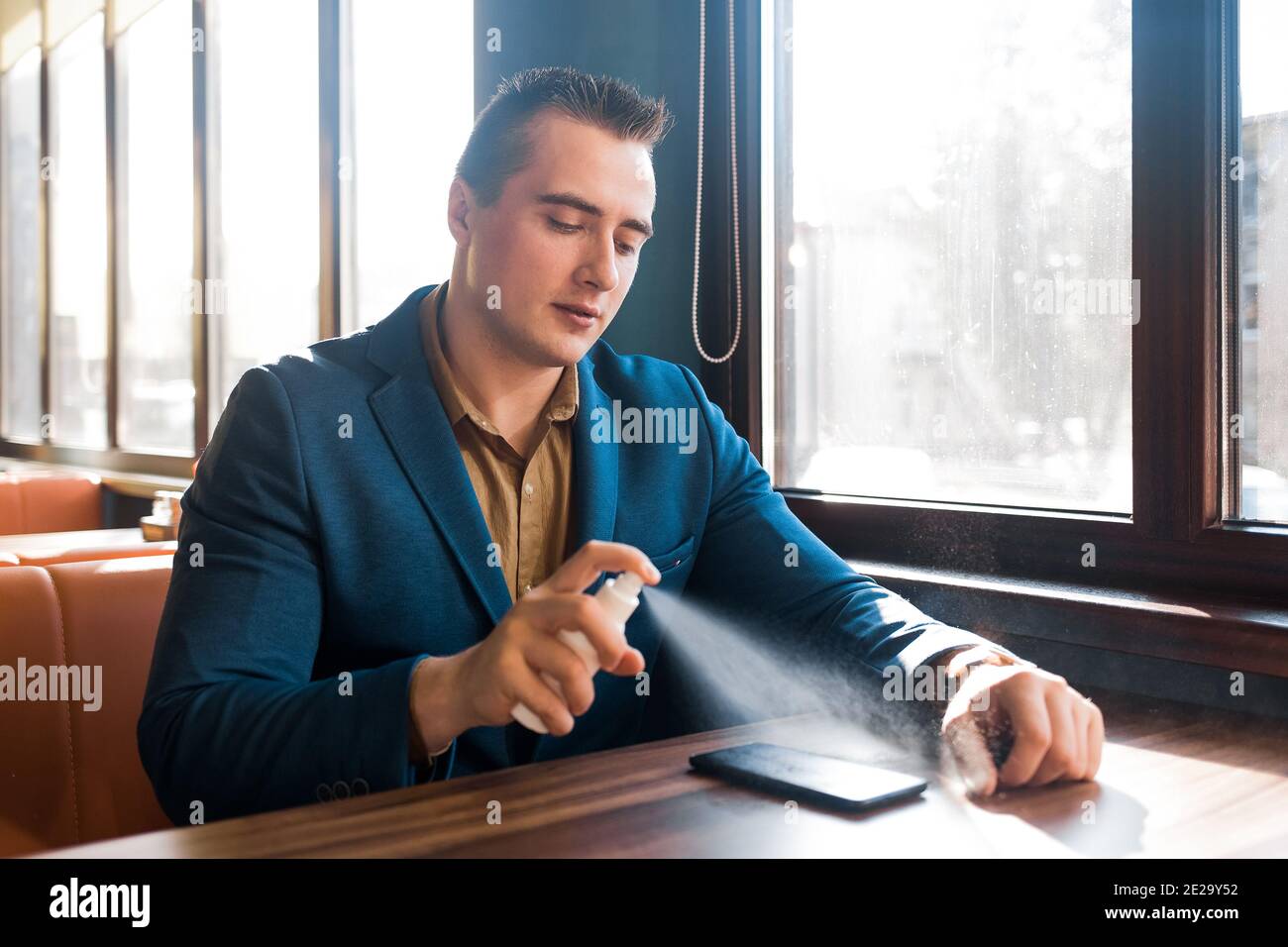 Giovane uomo d'affari caucasico in un vestito blu spruzzi un antisettico su un telefono cellulare. Foto Stock