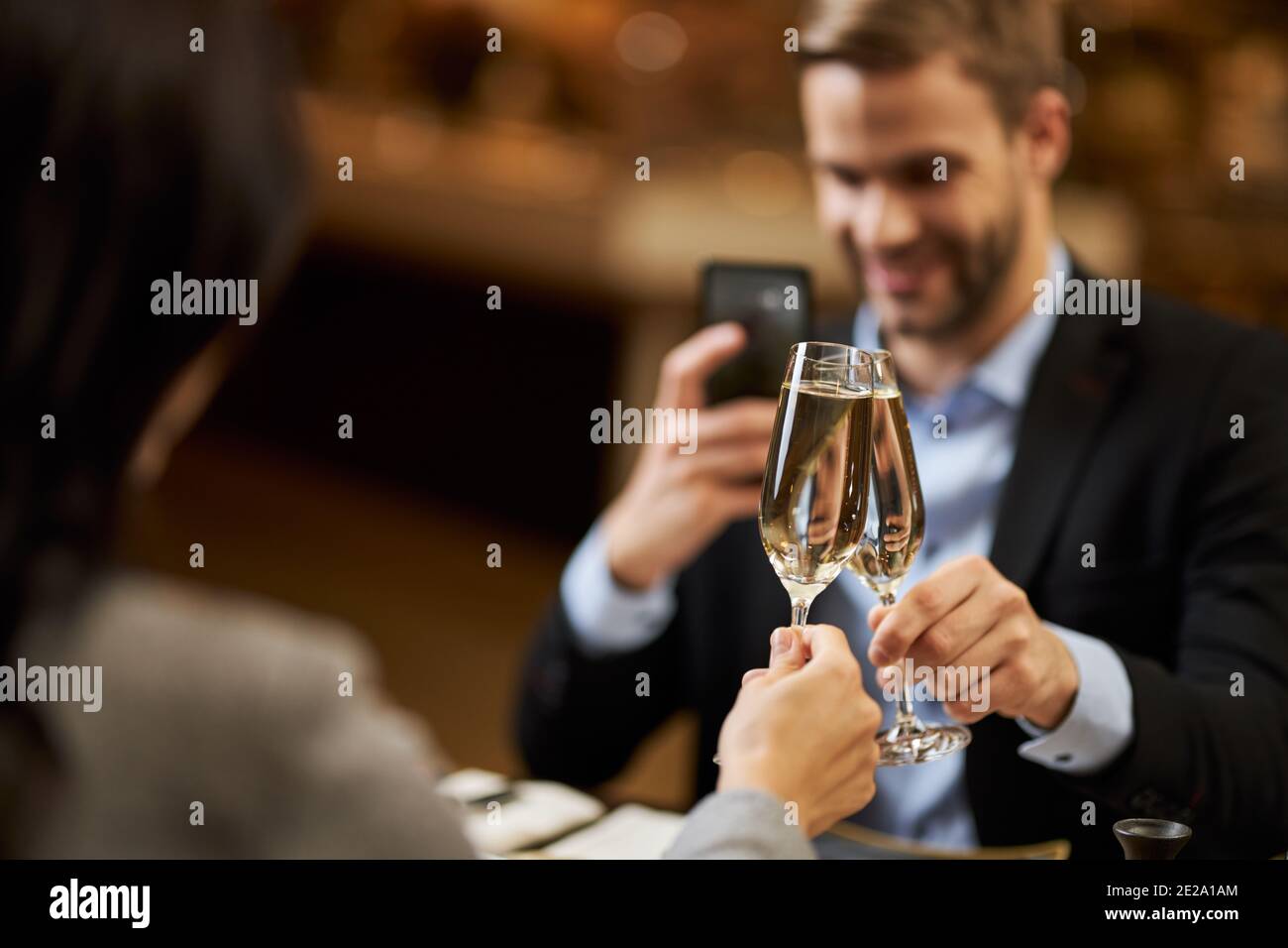 Foto a fuoco selettivo di bicchieri di champagne che si aggraffano con un bell'uomo scattare foto in background Foto Stock