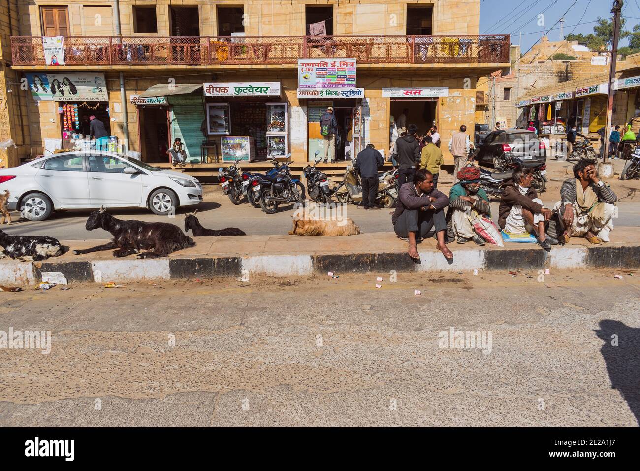 Jaisalmer, Rajasthan / India - 8 gennaio 2021 : la gente e le capre siedono su un divisorio stradale, la gente siede sul divisore nella luce solare diretta che aspetta la loro b Foto Stock