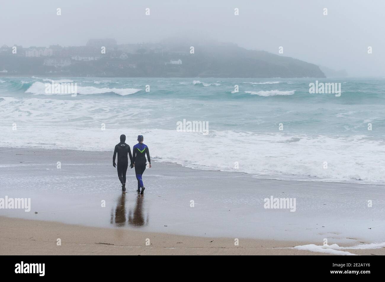 Due persone in mute che camminano lungo la costa in condizioni climatiche fredde e nebbie sulla Great Western Beach a Newquay in Cornovaglia. Foto Stock