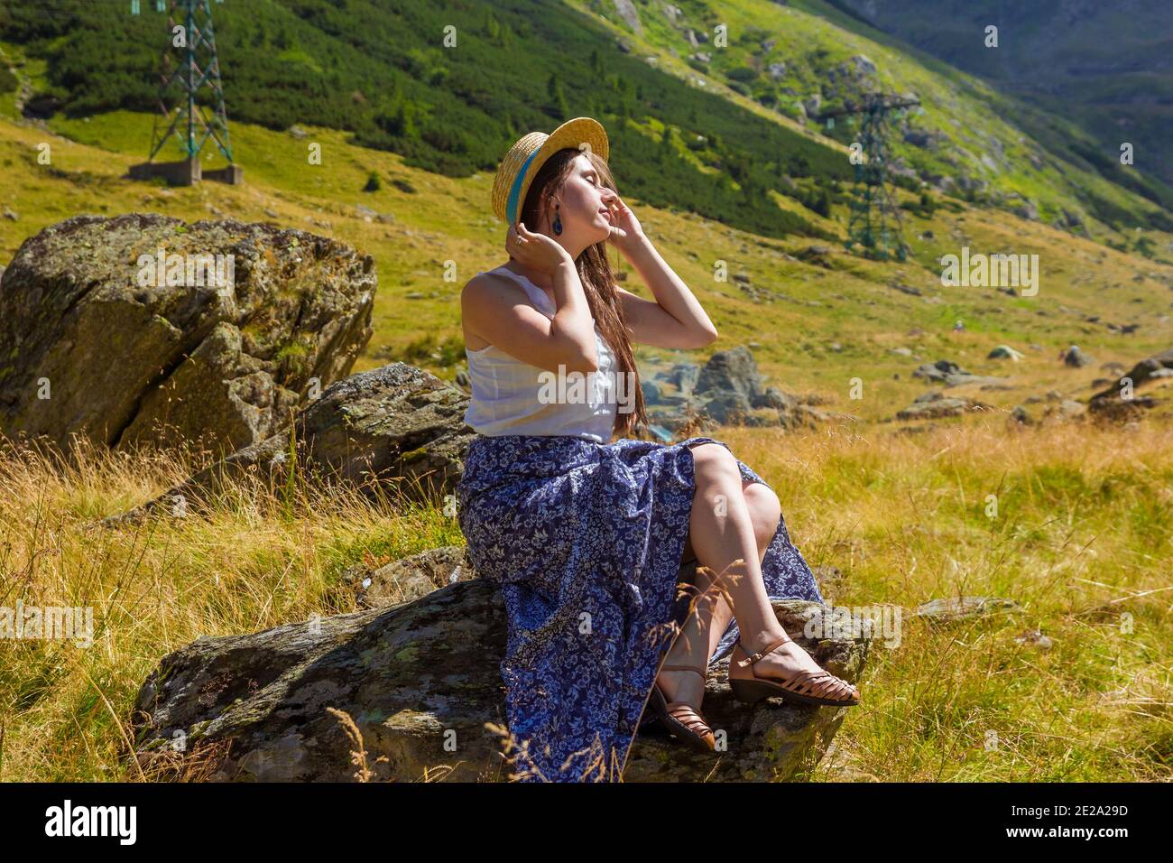 ragazza in abito si siede su una roccia che tiene una paglia cappello Foto Stock