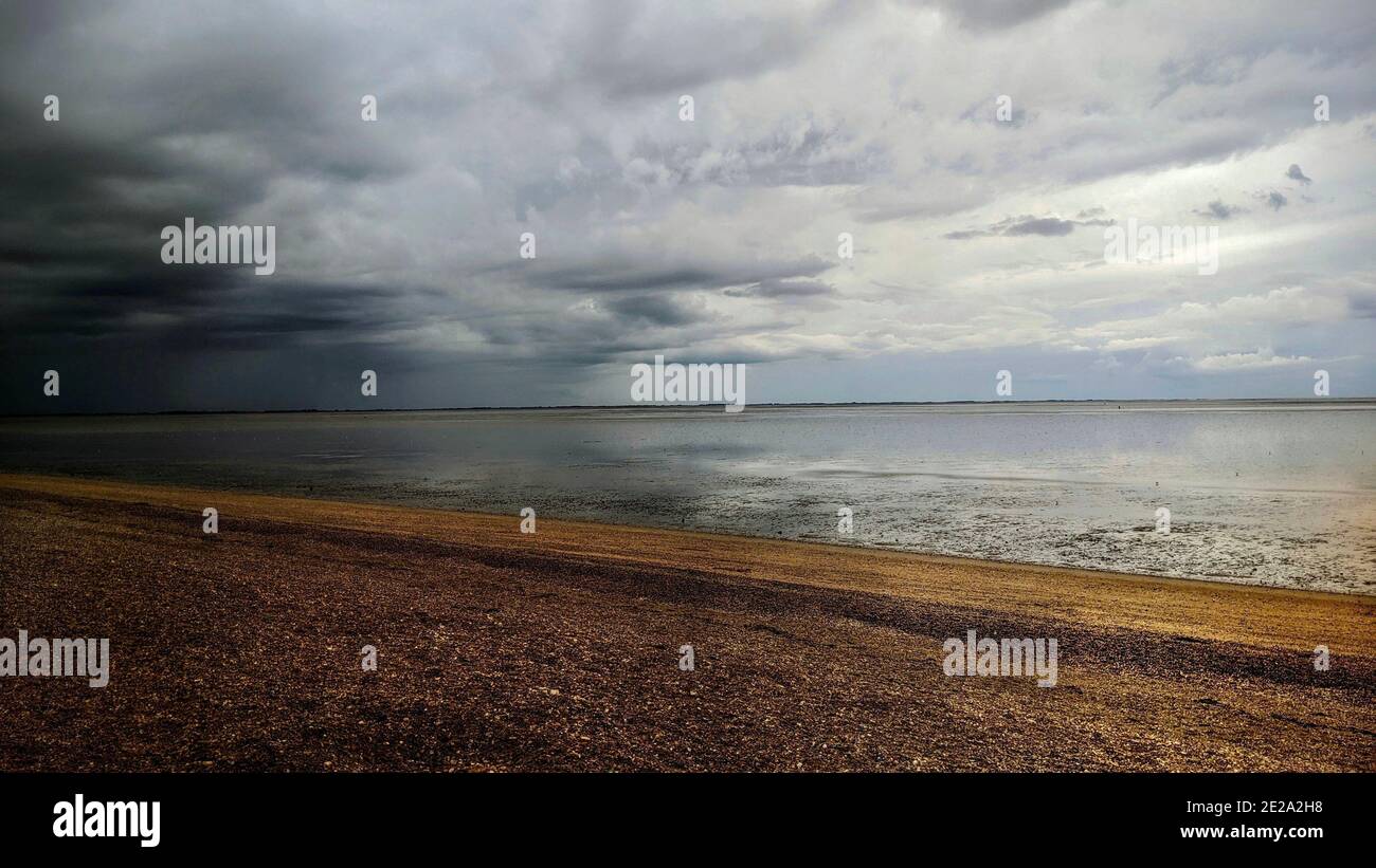 Le nuvole di tempesta grigio scuro si raccolgono su una spiaggia di ciottoli sulla costa di Norfolk. Stagcape di Snettisham Beach in una giornata di tempesta sul mare britannico. Foto Stock