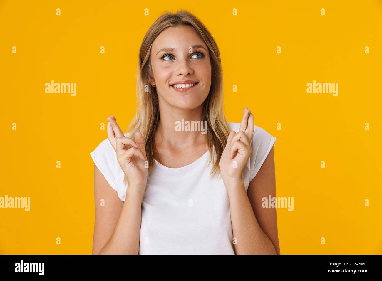 Felice bella ragazza che posa con le dita incrociate per buona fortuna isolato su sfondo giallo Foto Stock