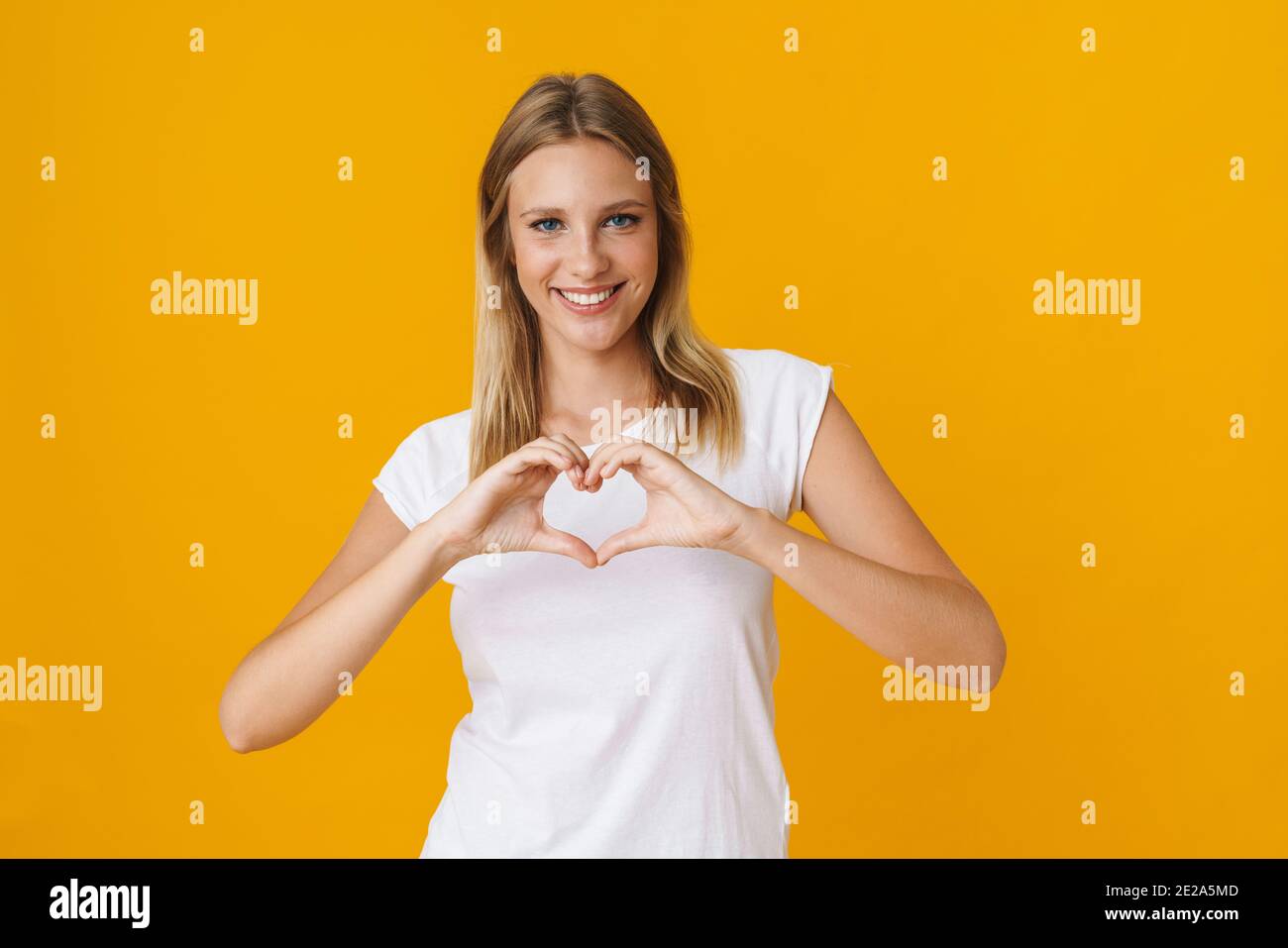 Felice bella ragazza che mostra il gesto del cuore con le dita isolate sopra sfondo giallo Foto Stock