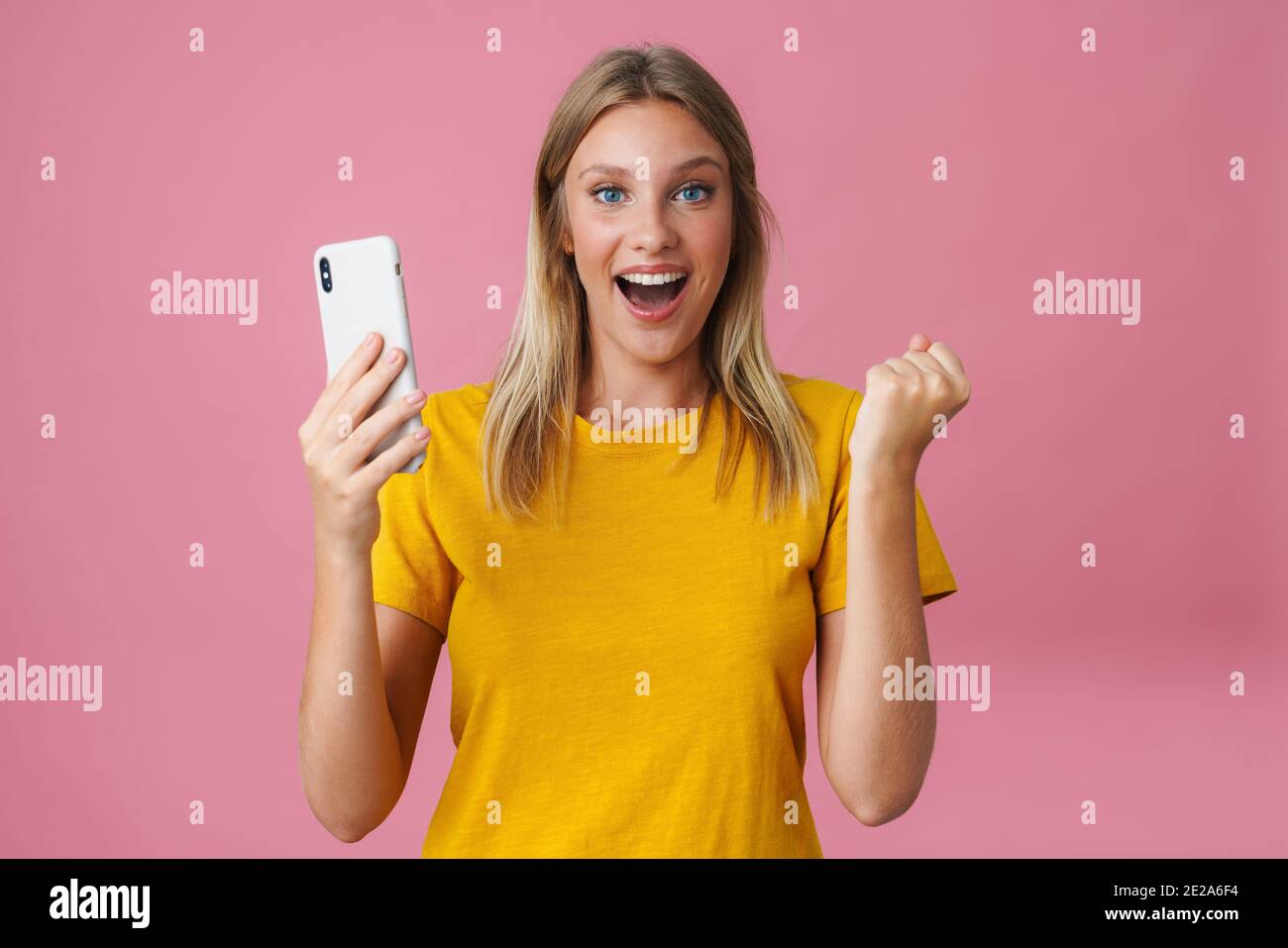 Ragazza eccitata facendo gesto vincitore mentre prendendo selfie sul cellulare isolato su sfondo rosa Foto Stock