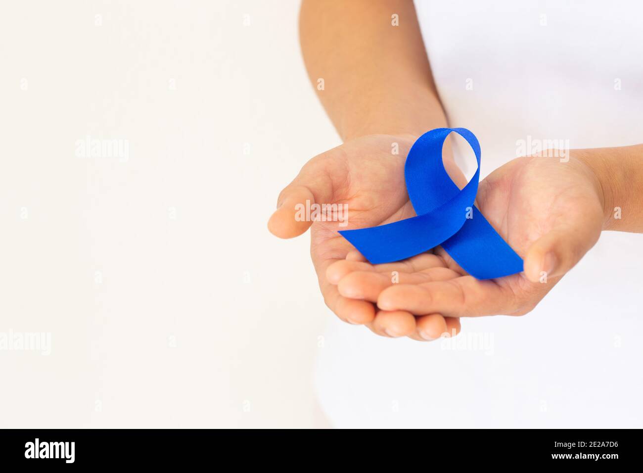 Mani che tengono il nastro blu profondo su tessuto bianco con spazio per la copia. Consapevolezza del cancro colorettale, cancro del colon della persona anziana e giornata mondiale del diabete, Chil Foto Stock