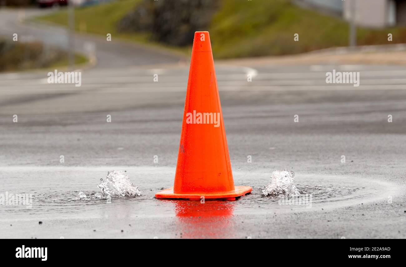 Un cono di strada arancione tra due piccole fontane d'acqua che bolle da buchi nella strada. L'acqua è pulita e pulita. Vista in primo piano. DOF poco profondo. Foto Stock