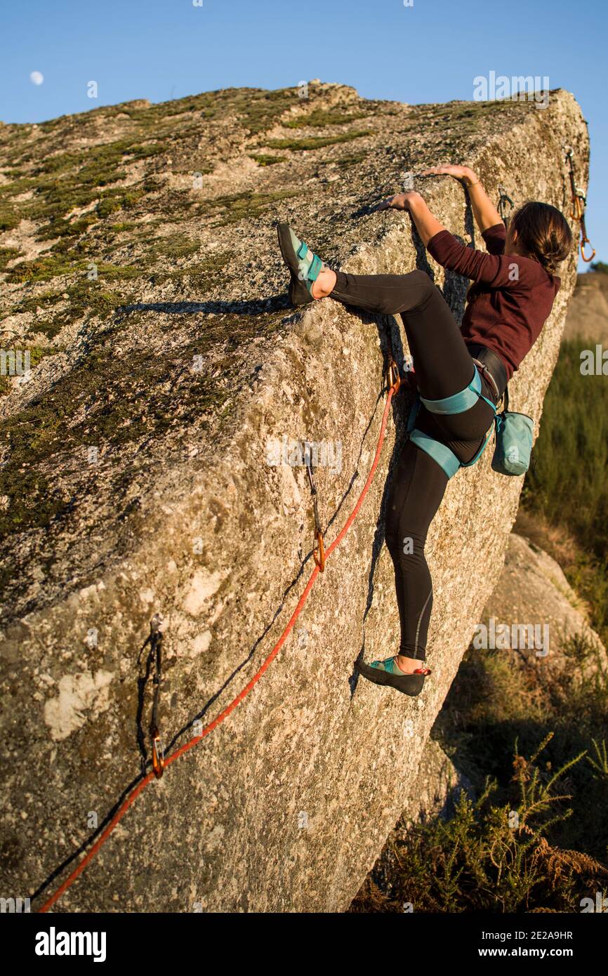 Ragazza che conduce sulla roccia che si arrampica, facendo un percorso orizzontale con la luna sullo sfondo Foto Stock