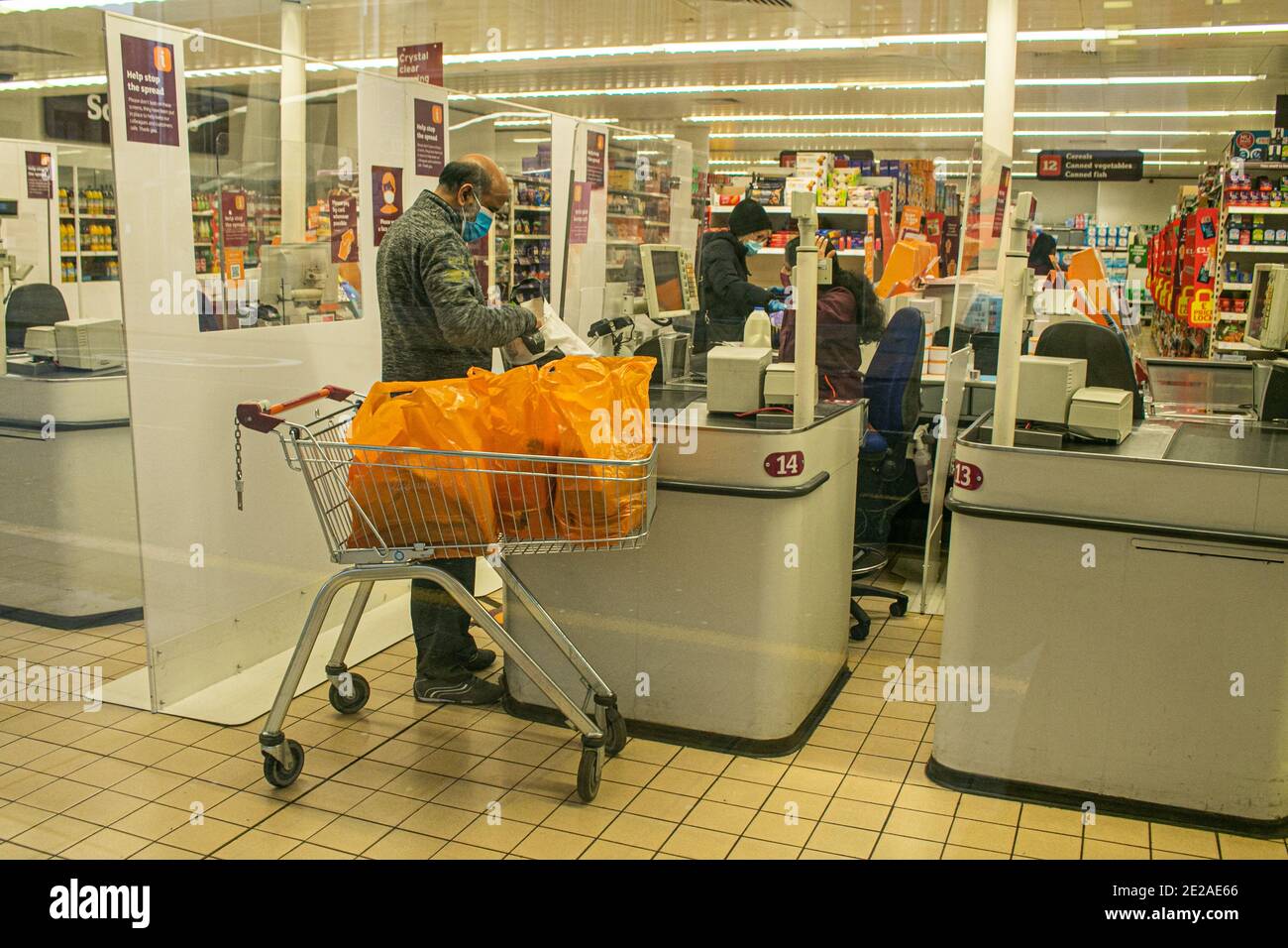 WIMBLEDON LONDRA, REGNO UNITO 13 GENNAIO 2021. Uno shopping che indossa un facemask con un trolley al banco del check out presso un Sainsburys a Wimbledon. I supermercati britannici Sainsbury's Morrisons e Tesco hanno annunciato che stanno applicando le regole sull'uso di maschere nei loro negozi come risposta diretta alle preoccupazioni circa il comportamento del pubblico durante lo shopping all'interno dei supermercati .. Credit: amer Ghazzal/Alamy Live News Foto Stock