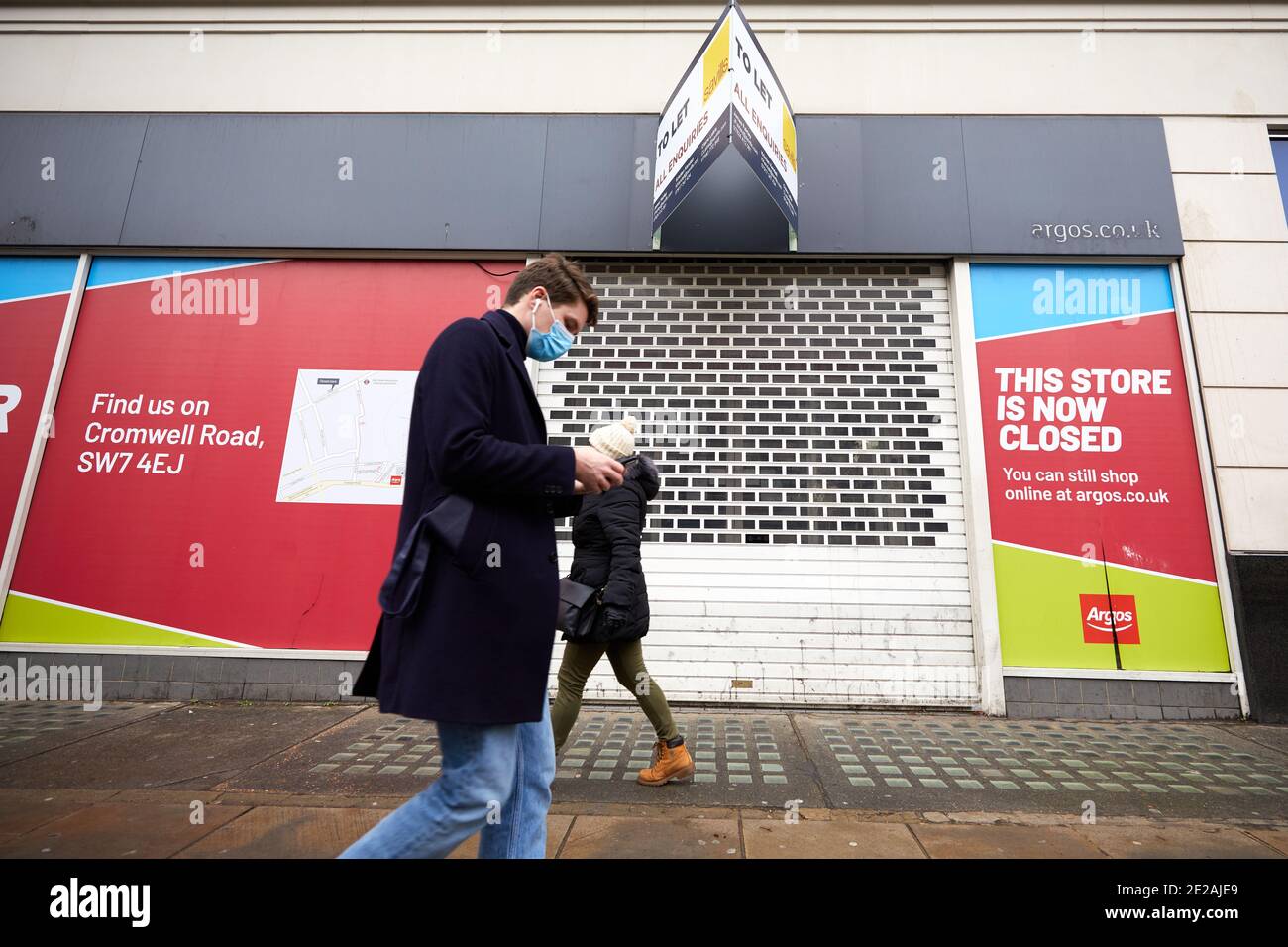 Londra, Regno Unito. - 12 Gen 2021: Un pedone mascherato passa davanti all'ex negozio Argos su Kensington High Street. Questo negozio è stato uno dei 125 negozi che la casa madre Sainsbury's ha recentemente annunciato di voler chiudere in tutto il Regno Unito. Foto Stock