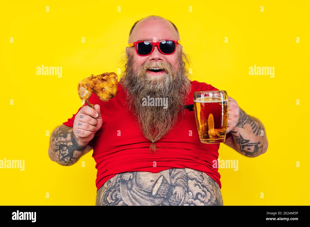 Uomo che guarda la televisione mentre beve e mangia. Divertente ritratto dell'uomo hipster su uno sfondo colorato Foto Stock