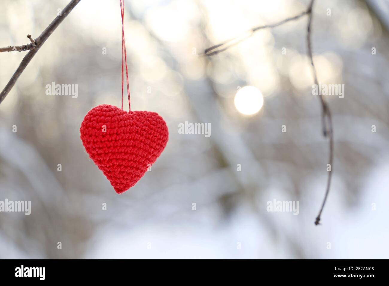 Cuore di San Valentino nella foresta invernale contro il sole. Cuore lavorato a maglia rosso appeso su un ramo, simbolo di amore romantico, sfondo per la vacanza sulla neve Foto Stock