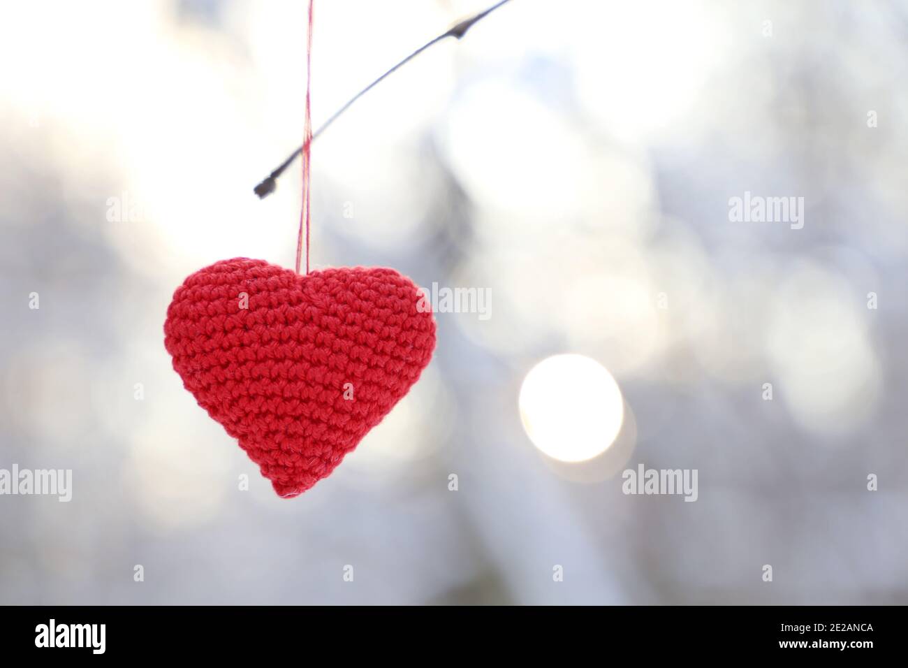 Cuore di San Valentino nella foresta invernale contro il sole. Cuore lavorato a maglia rosso appeso su un ramo, simbolo di amore romantico, sfondo per la vacanza sulla neve Foto Stock