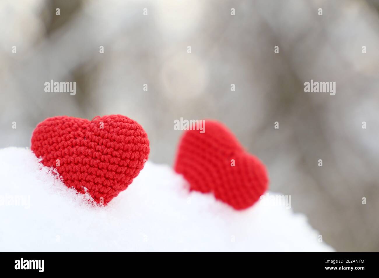 Cuori di San Valentino nella foresta invernale alla luce del sole. Due cuori rossi in maglia sulla neve, simbolo di amore romantico, sfondo per le vacanze Foto Stock