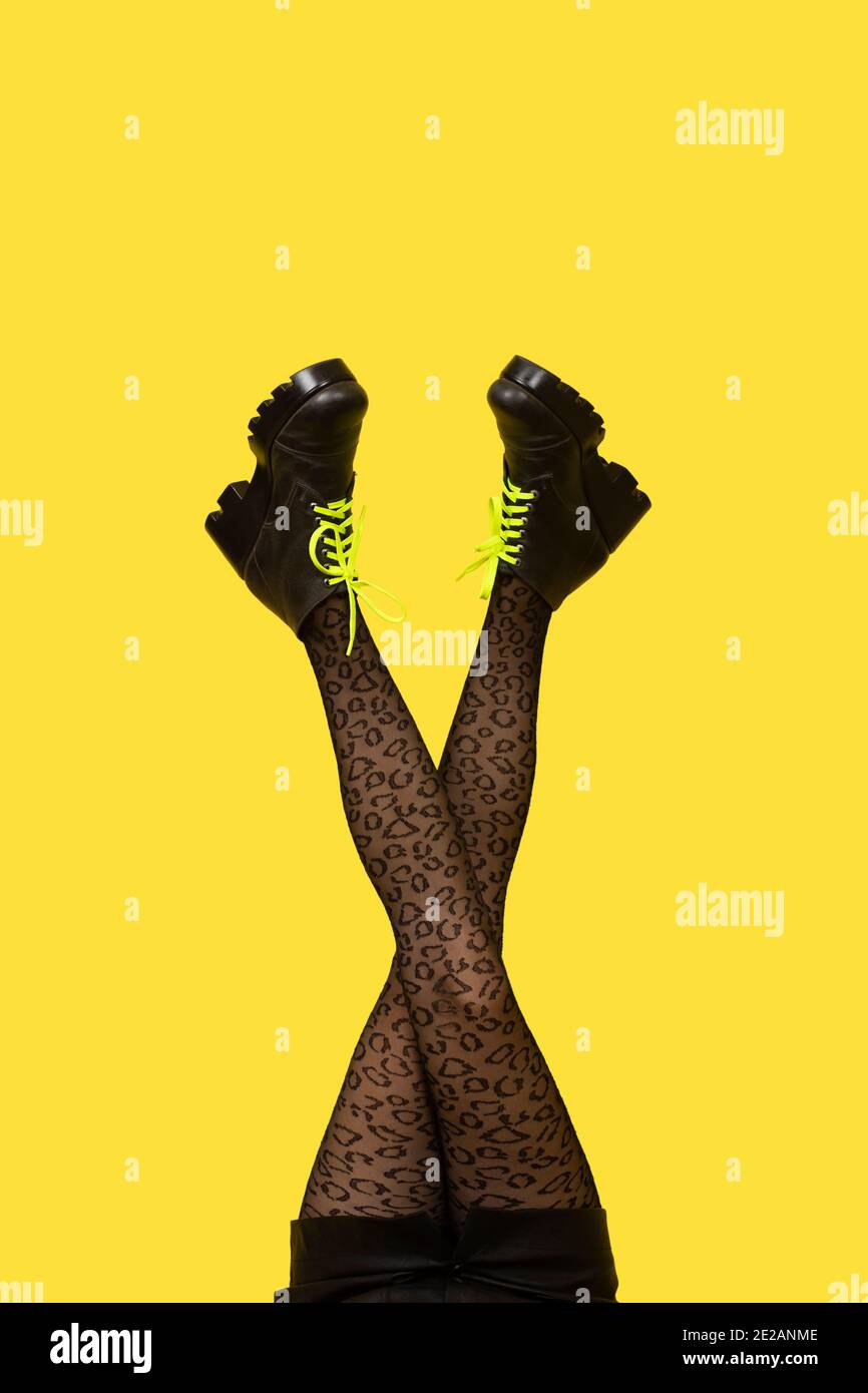 Nuovi stivali grigi femmina con lacci gialli luminosi su lunghe gambe incrociate donna snella in collant grigio isolato su sfondo giallo. Concetto di pop art con H Foto Stock