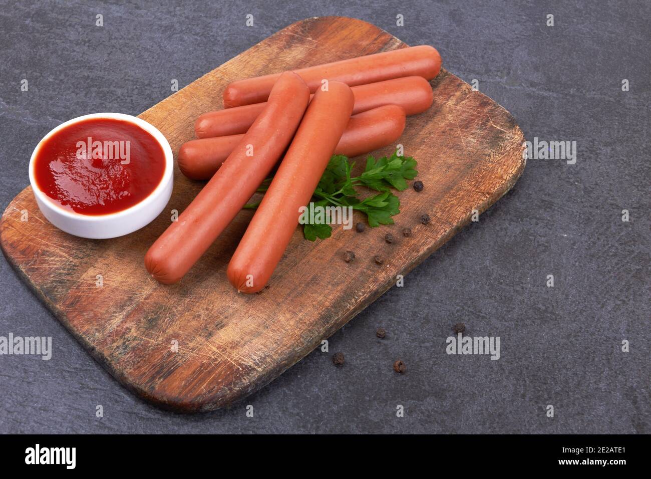 Salsicce di frankfurter crude con ketchup sul tagliere Foto Stock