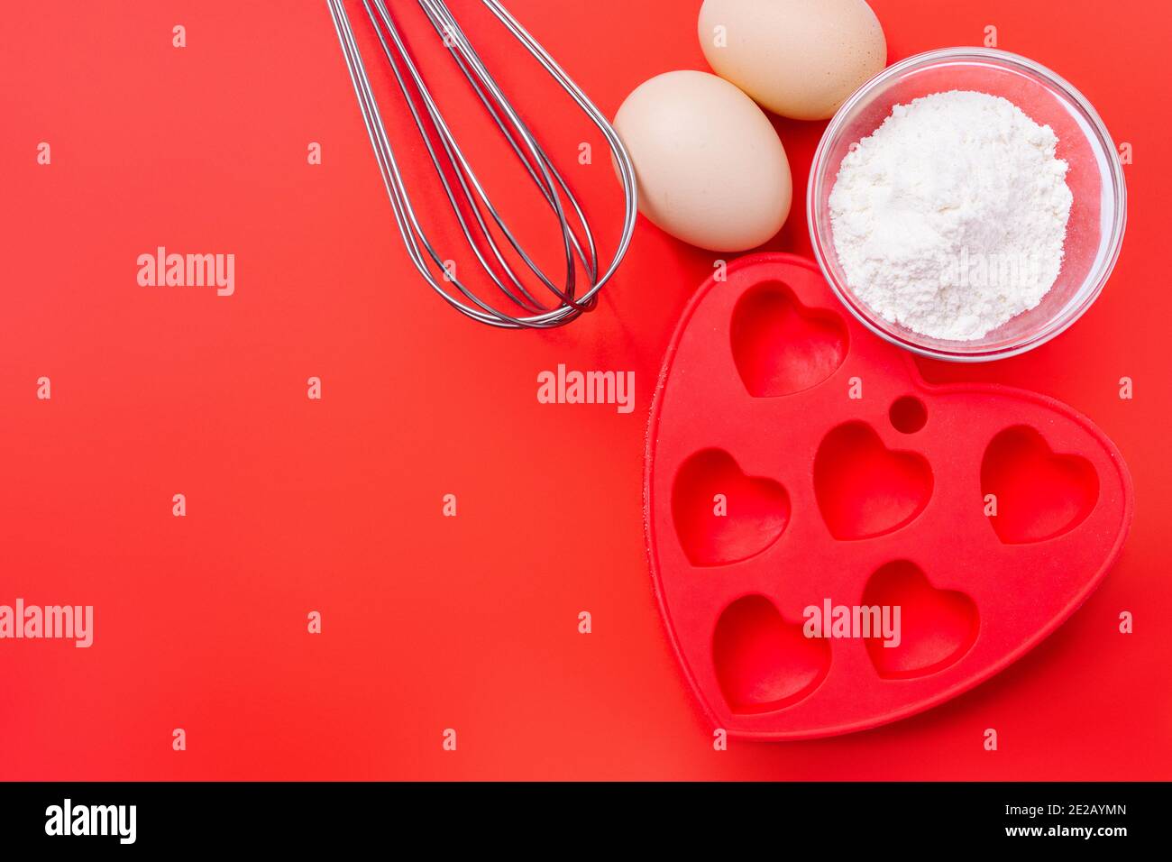 Frusta, muffa in silicone rosso e ingredienti per un dessert su un tavolo festivo il giorno di San Valentino. Foto Stock