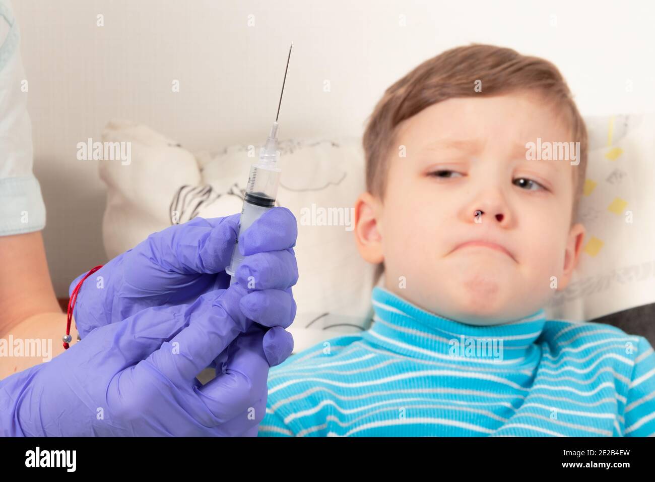 un medico in guanti medici blu inietta un bambino malato con una siringa Foto Stock