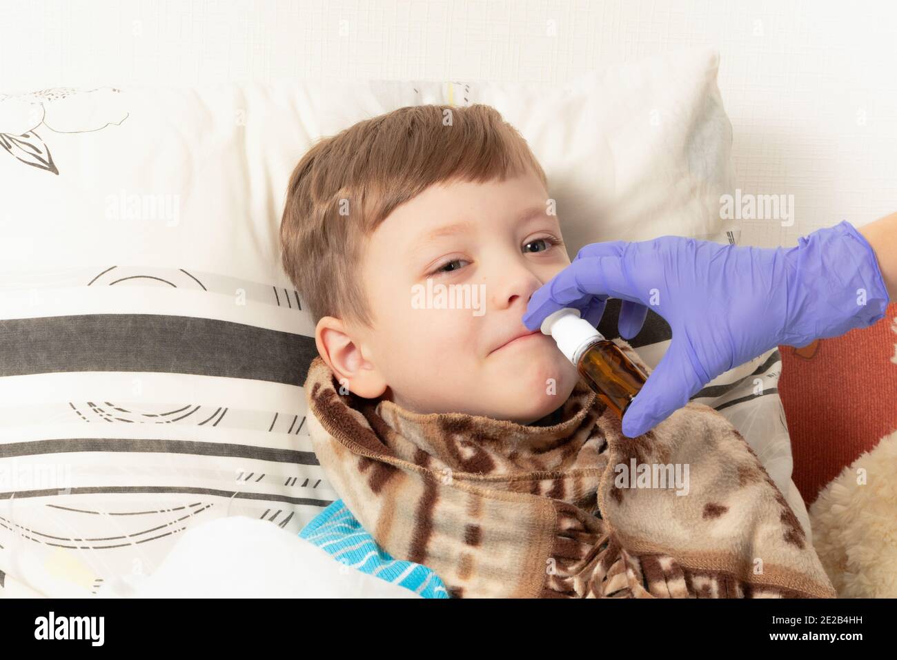 la mamma nei guanti medici blu spruzza la medicina nel naso di un bambino malato Foto Stock