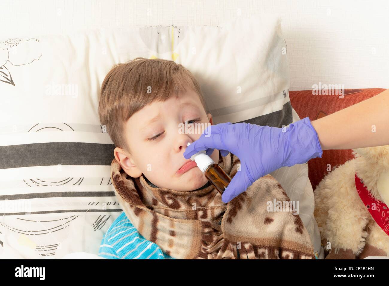 la mamma nei guanti medici blu spruzza la medicina nel naso di un bambino malato Foto Stock
