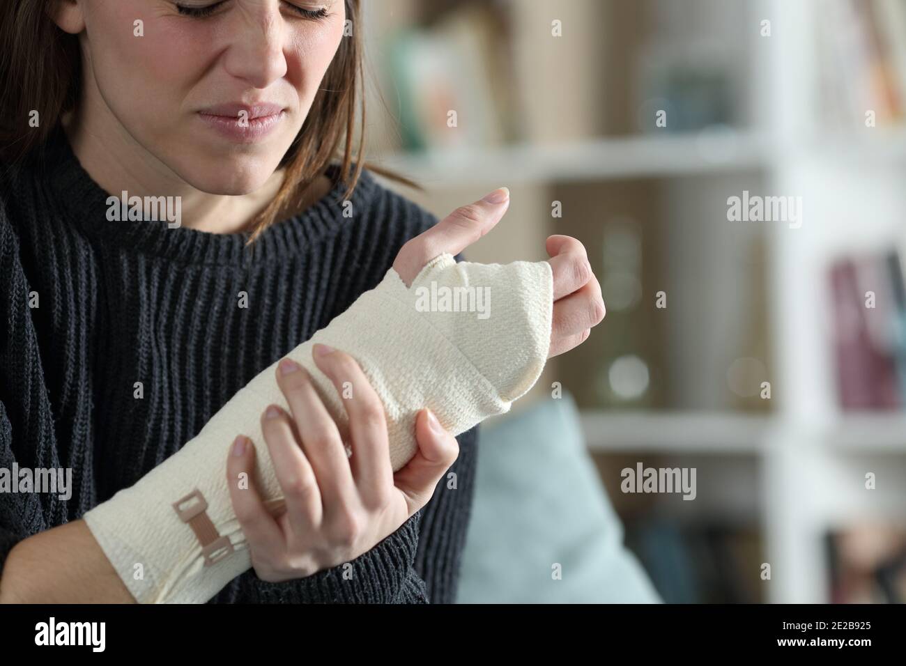 Triste donna ferita che lamenta di indossare braccio bandito in vita camera a casa Foto Stock