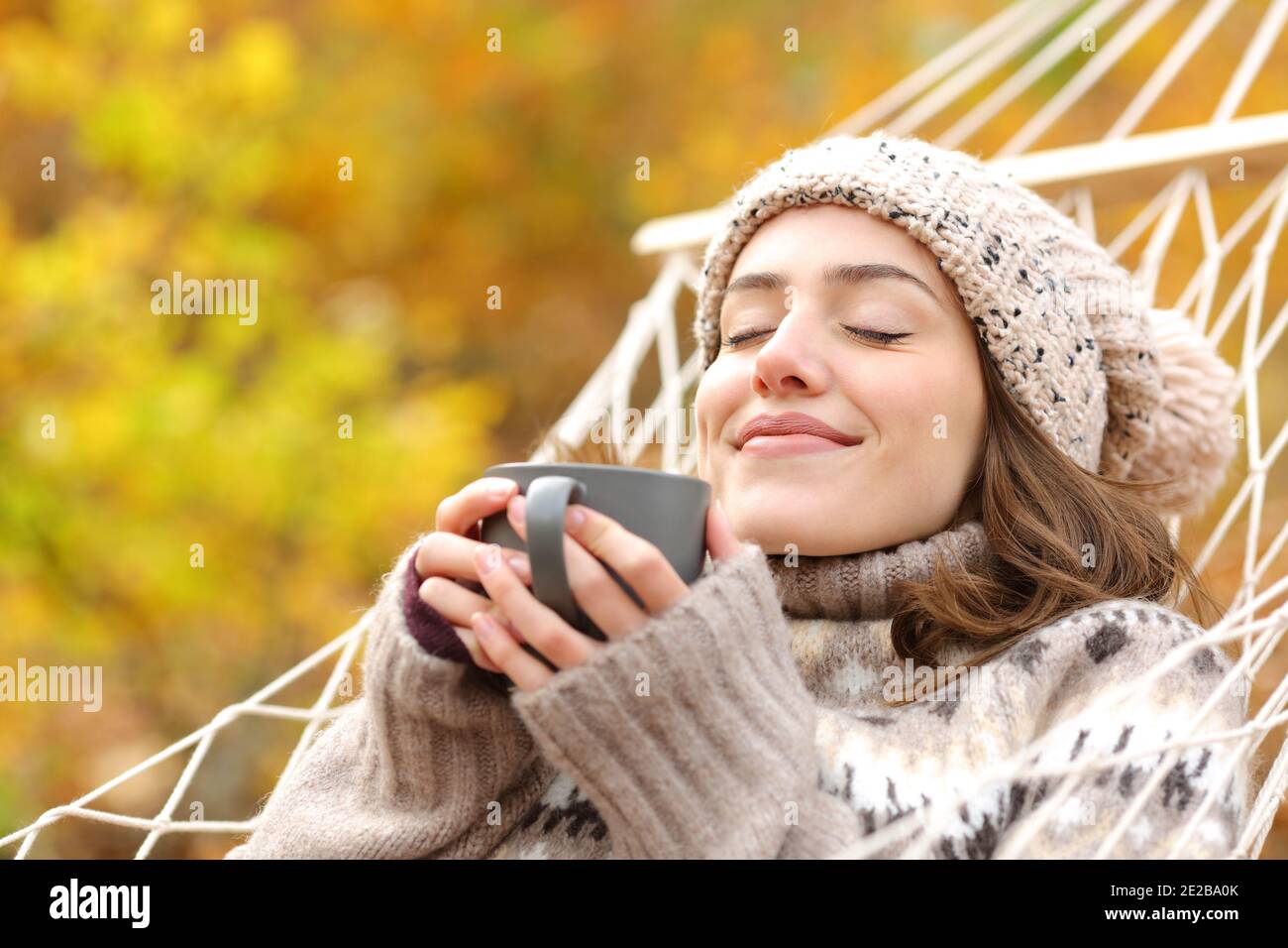 Donna rilassata che odora il caffè sdraiato sull'amaca nelle vacanze autunnali Foto Stock