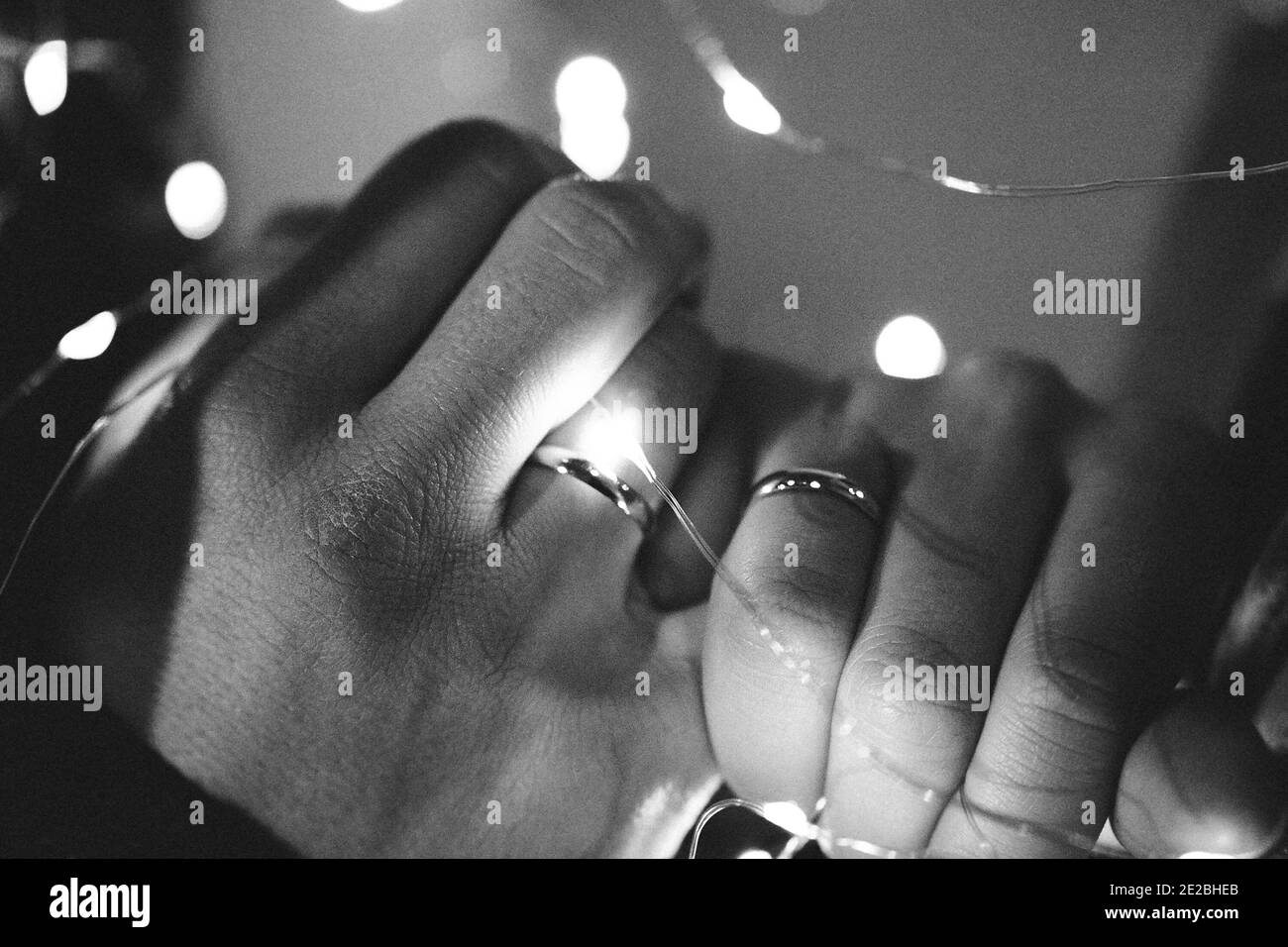 due mani, quella di un uomo e quella di una donna, sono legate da una ghirlanda di luci: mani con anelli, concetto di matrimonio, fotografia granulosa Foto Stock