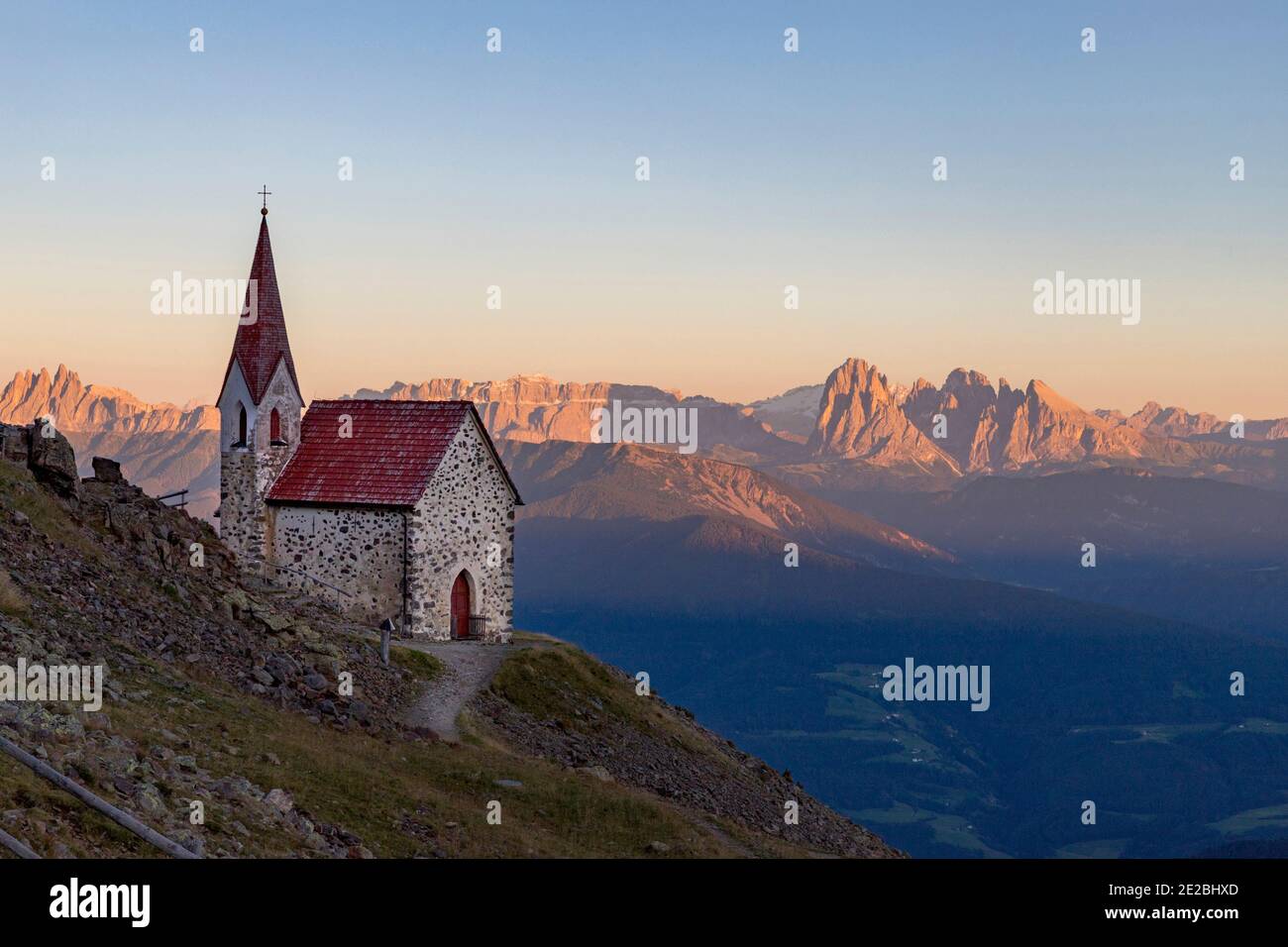 Piccola cappella e vista sulla catena montuosa delle Dolomiti illuminate d'arancio al tramonto d'estate, Alto Adige, Italia Foto Stock