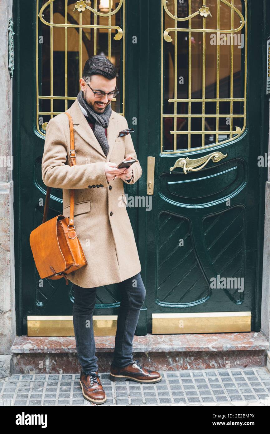 Elegante giovane uomo in stile dandy con lo smart telefono sulla porta anteriore Foto Stock