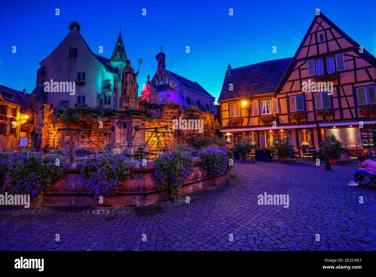 La piazza principale del villaggio feudale di Eguisheim con case a graticcio, vecchia fontana e una chiesa. Foto scattata il 10 agosto 2019 nell'es Foto Stock