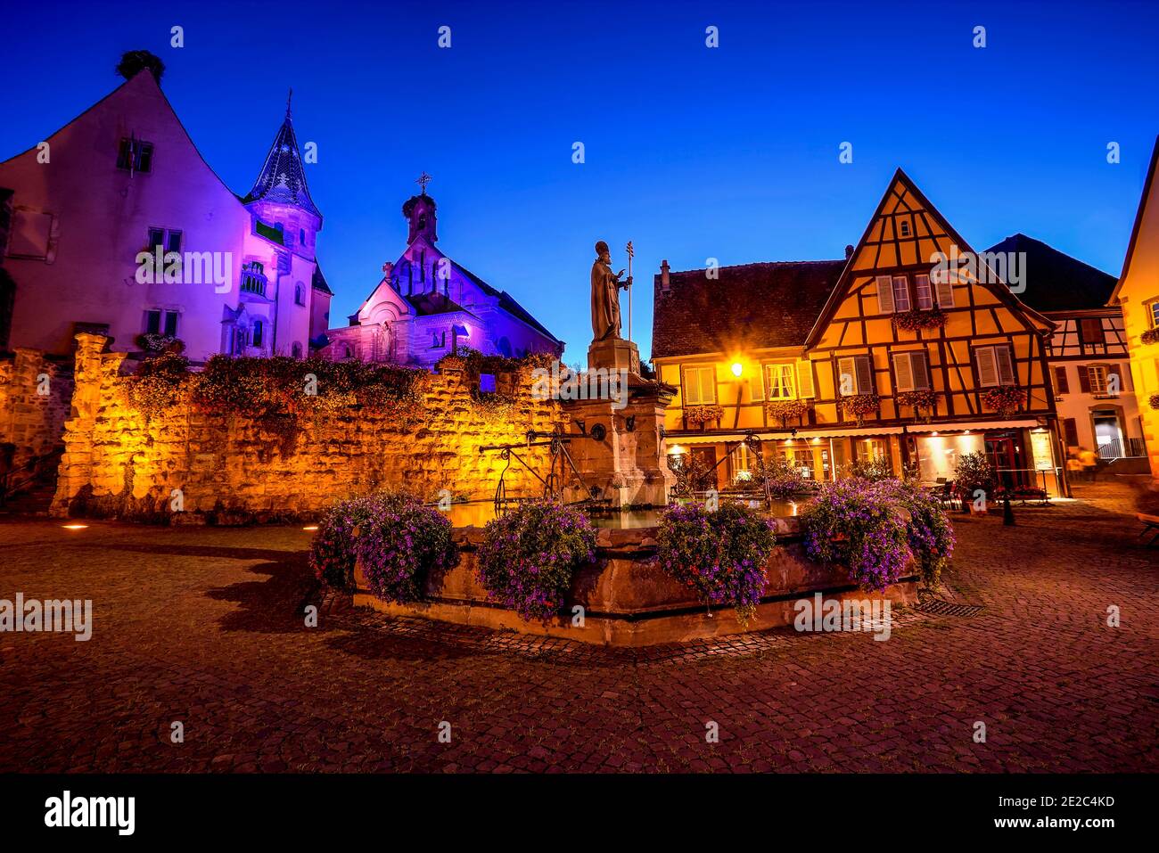 La piazza principale del villaggio feudale di Eguisheim con case a graticcio, vecchia fontana e una chiesa. Foto scattata il 10 agosto 2019 nell'es Foto Stock